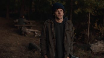 Movie still from “Night Moves” (2013), directed by Kelly Reichardt – A man in a hat and jacket standing in the woods; Medium shot, Over the shoulder angle