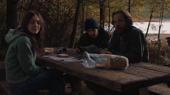 Movie still from “Night Moves” (2013), directed by Kelly Reichardt – A group of people sitting at a picnic table in the woods; Medium shot, Over the shoulder angle