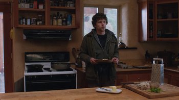 Movie still from “Night Moves” (2013), directed by Kelly Reichardt – A man standing in a kitchen holding a plate; Medium shot, Low angle