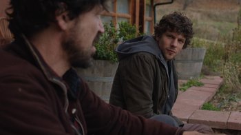 Movie still from “Night Moves” (2013), directed by Kelly Reichardt – Two men sitting on the ground in front of a building; Medium shot, Over the shoulder angle