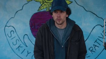 Movie still from “Night Moves” (2013), directed by Kelly Reichardt – A man in a baseball cap standing in front of a mural; Close Up shot, Low angle