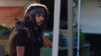 Movie still from “Night Moves” (2013), directed by Kelly Reichardt – A man with dreads is standing in front of a fence; Medium shot, Over the shoulder angle