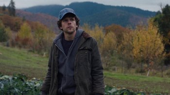 Movie still from “Night Moves” (2013), directed by Kelly Reichardt – A man in a field wearing a hat and jacket; Medium shot, Over the shoulder angle