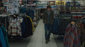 Movie still from “Night Moves” (2013), directed by Kelly Reichardt – A man walking down the aisle of a clothing store; Wide shot, Over the shoulder angle