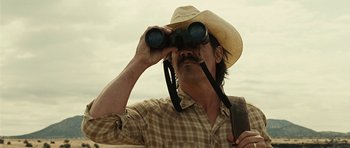 Movie still from “No Country for Old Men” (2007), directed by Joel Coen – A man in a cowboy hat looking through binoculars; Close Up shot, Low angle