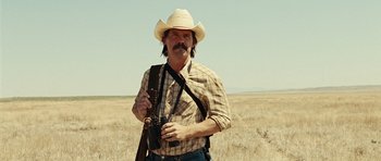 Movie still from “No Country for Old Men” (2007), directed by Joel Coen – A man in a cowboy hat holding a camera; Medium shot, Low angle