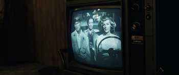 Movie still from “No Country for Old Men” (2007), directed by Joel Coen – A television screen showing a man and two women in a car; Close Up shot, Over the shoulder angle