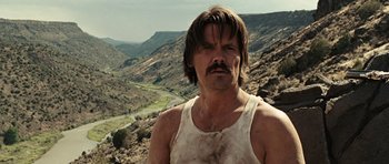 Movie still from “No Country for Old Men” (2007), directed by Joel Coen – A man with a mustache standing on top of a mountain; Close Up shot, Over the shoulder angle