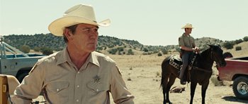 Movie still from “No Country for Old Men” (2007), directed by Joel Coen – A man wearing a cowboy hat standing next to a horse in the desert; Medium shot, Over the shoulder angle