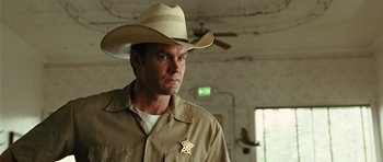 Movie still from “No Country for Old Men” (2007), directed by Joel Coen – A man wearing a cowboy hat with a sheriff badge on it; Close Up shot, Low angle