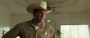 Movie still from “No Country for Old Men” (2007), directed by Joel Coen – A man wearing a cowboy hat and a sheriff badge; Close Up shot, Low angle
