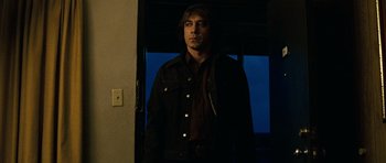 Movie still from “No Country for Old Men” (2007), directed by Joel Coen – A man standing in front of a window in the dark; Medium shot, Low angle