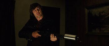 Movie still from “No Country for Old Men” (2007), directed by Joel Coen – A man holding a gun in a dark room; Medium shot, Low angle