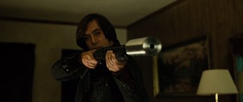 Movie still from “No Country for Old Men” (2007), directed by Joel Coen – A man holding a gun in a room; Medium shot, Low angle