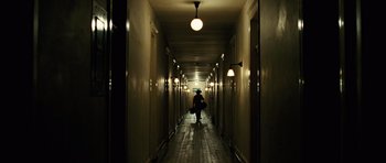 Movie still from “No Country for Old Men” (2007), directed by Joel Coen – A person walking down a long hallway with lights on; Wide shot, High angle