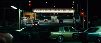 Movie still from “No Country for Old Men” (2007), directed by Joel Coen – Cars are stopped at the united states border station at night; Extreme Wide shot, Low angle
