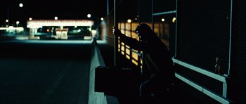 Movie still from “No Country for Old Men” (2007), directed by Joel Coen – A person sitting on a bench at night; Wide shot, Low angle