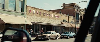 Movie still from “No Country for Old Men” (2007), directed by Joel Coen – People are walking on the sidewalk in front of a store; Wide shot, Low angle