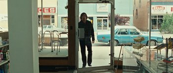 Movie still from “No Country for Old Men” (2007), directed by Joel Coen – A man standing in front of an open glass door; Wide shot, Over the shoulder angle