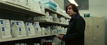 Movie still from “No Country for Old Men” (2007), directed by Joel Coen – A man is holding something in his hand in a store; Medium shot, Low angle