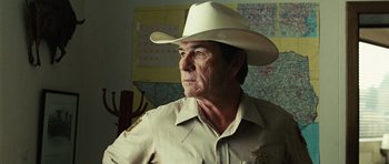 Movie still from “No Country for Old Men” (2007), directed by Joel Coen – A man wearing a white cowboy hat and uniform; Close Up shot, Over the shoulder angle