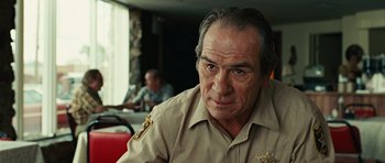 Movie still from “No Country for Old Men” (2007), directed by Joel Coen – An older man in a sheriff's uniform stares into the camera; Close Up shot, Over the shoulder angle