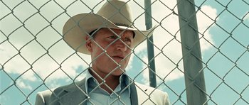 Movie still from “No Country for Old Men” (2007), directed by Joel Coen – A man wearing a cowboy hat standing in front of a chain link fence; Close Up shot, Low angle