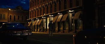 Movie still from “No Country for Old Men” (2007), directed by Joel Coen – A person riding a bike down a street at night; Wide shot, Low angle