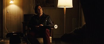 Movie still from “No Country for Old Men” (2007), directed by Joel Coen – A man sitting in front of a lamp in a room; Medium shot, Over the shoulder angle