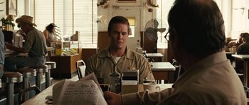 Movie still from “No Country for Old Men” (2007), directed by Joel Coen – A man sitting in front of another man holding a newspaper; Medium shot, Over the shoulder angle