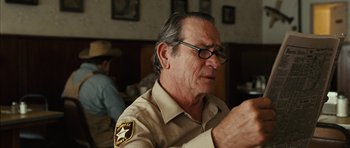 Movie still from “No Country for Old Men” (2007), directed by Joel Coen – An older man wearing a sheriff's uniform looking at his cell phone; Close Up shot, Over the shoulder angle