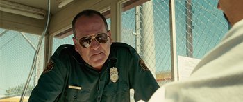 Movie still from “No Country for Old Men” (2007), directed by Joel Coen – A police officer wearing sunglasses and a green uniform; Close Up shot, Low angle