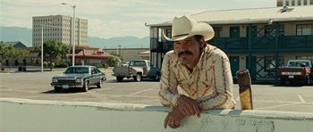 Movie still from “No Country for Old Men” (2007), directed by Joel Coen – A man wearing a cowboy hat leaning on a wall in a parking lot; Medium shot, Over the shoulder angle