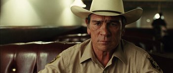Movie still from “No Country for Old Men” (2007), directed by Joel Coen – A person wearing a cowboy hat; Close Up shot, Over the shoulder angle