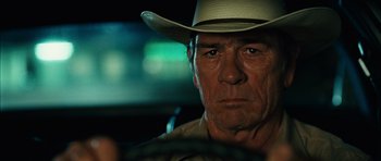 Movie still from “No Country for Old Men” (2007), directed by Joel Coen – A person wearing a hat in a car; Close Up shot, Over the shoulder angle