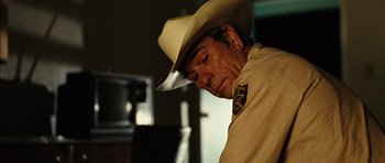 Movie still from “No Country for Old Men” (2007), directed by Joel Coen – A man wearing a cowboy hat looking down at the ground; Close Up shot, Over the shoulder angle