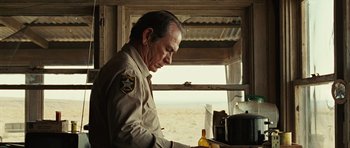 Movie still from “No Country for Old Men” (2007), directed by Joel Coen – An old man in uniform looking down at a bottle; Medium shot, Over the shoulder angle