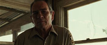Movie still from “No Country for Old Men” (2007), directed by Joel Coen – A person wearing a uniform; Close Up shot, Over the shoulder angle