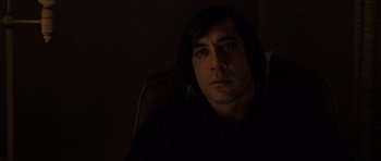 Movie still from “No Country for Old Men” (2007), directed by Joel Coen – A man sitting in a chair in a dark room; Close Up shot, Low angle