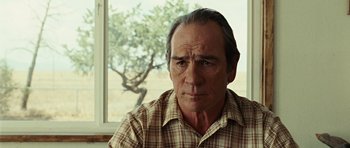 Movie still from “No Country for Old Men” (2007), directed by Joel Coen – An older man in a plaid shirt looking at the camera; Close Up shot, Over the shoulder angle