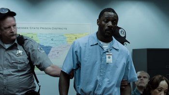 Movie still from “No Good Deed” (2014), directed by Sam Miller – A man in a blue prison uniform standing in front of a map; Medium shot, Over the shoulder angle