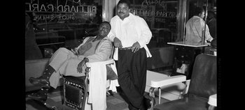 Movie still from “No Sudden Move” (2021), directed by Steven Soderbergh – A man standing next to another man on a chair; Medium shot, Low angle