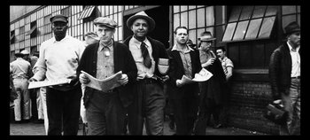 Movie still from “No Sudden Move” (2021), directed by Steven Soderbergh – A black and white photo of a group of men holding newspapers; Medium shot, Low angle