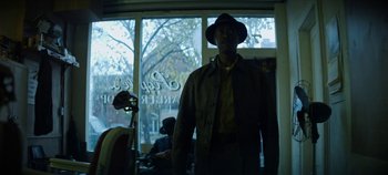 Movie still from “No Sudden Move” (2021), directed by Steven Soderbergh – A man standing in front of a window wearing a hat; Medium shot, Low angle