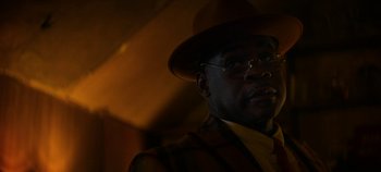 Movie still from “No Sudden Move” (2021), directed by Steven Soderbergh – A man wearing a hat and glasses in the dark; Close Up shot, Low angle