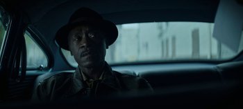 Movie still from “No Sudden Move” (2021), directed by Steven Soderbergh – A man sitting in the back seat of a car wearing a hat; Close Up shot, Over the shoulder angle