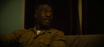 Movie still from “No Sudden Move” (2021), directed by Steven Soderbergh – An older man sitting on a couch in a room; Close Up shot, Low angle