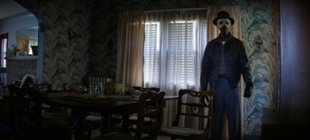 Movie still from “No Sudden Move” (2021), directed by Steven Soderbergh – A person with a mask standing in front of a table; Medium shot, Low angle