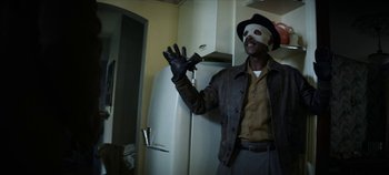Movie still from “No Sudden Move” (2021), directed by Steven Soderbergh – A man wearing a mask and gloves in a kitchen; Medium shot, Low angle