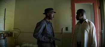 Movie still from “No Sudden Move” (2021), directed by Steven Soderbergh – A man holding a gun while standing next to a wall; Medium shot, Over the shoulder angle